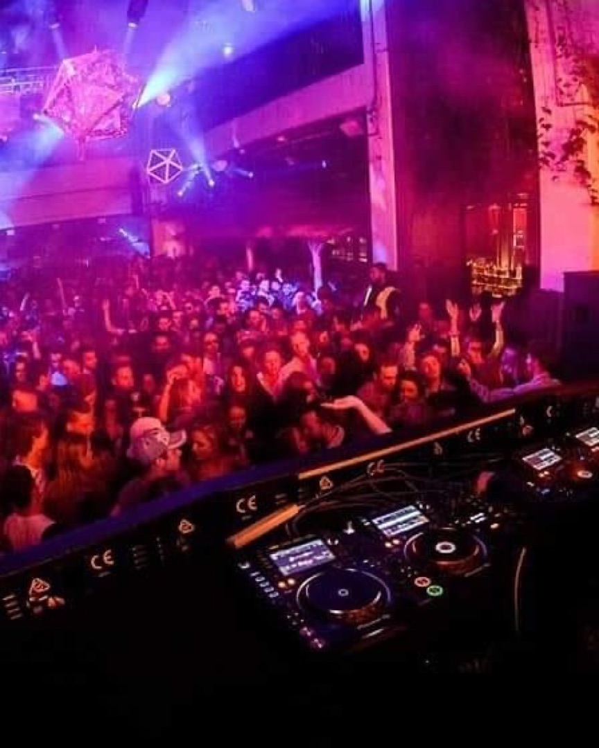 A packed club under purple lights, seen from the DJ booth